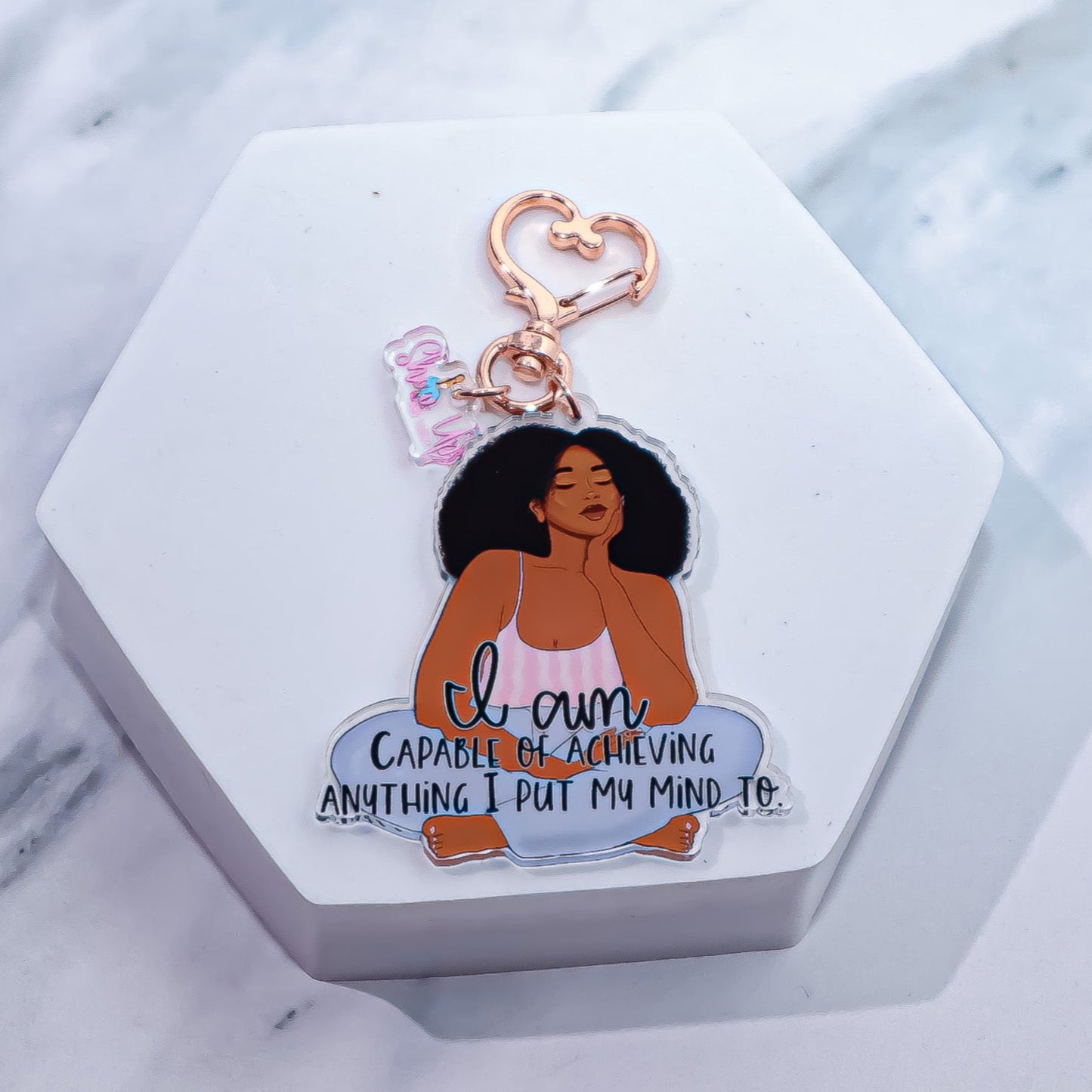 "I Am Capable" Acrylic Keychain featuring a bold illustration of a Black woman with natural hair, sitting confidently, paired with the motivational affirmation "I am capable of achieving anything I put my mind to." Designed with rose gold hardware and a heart-shaped clasp, perfect for keys or bags.